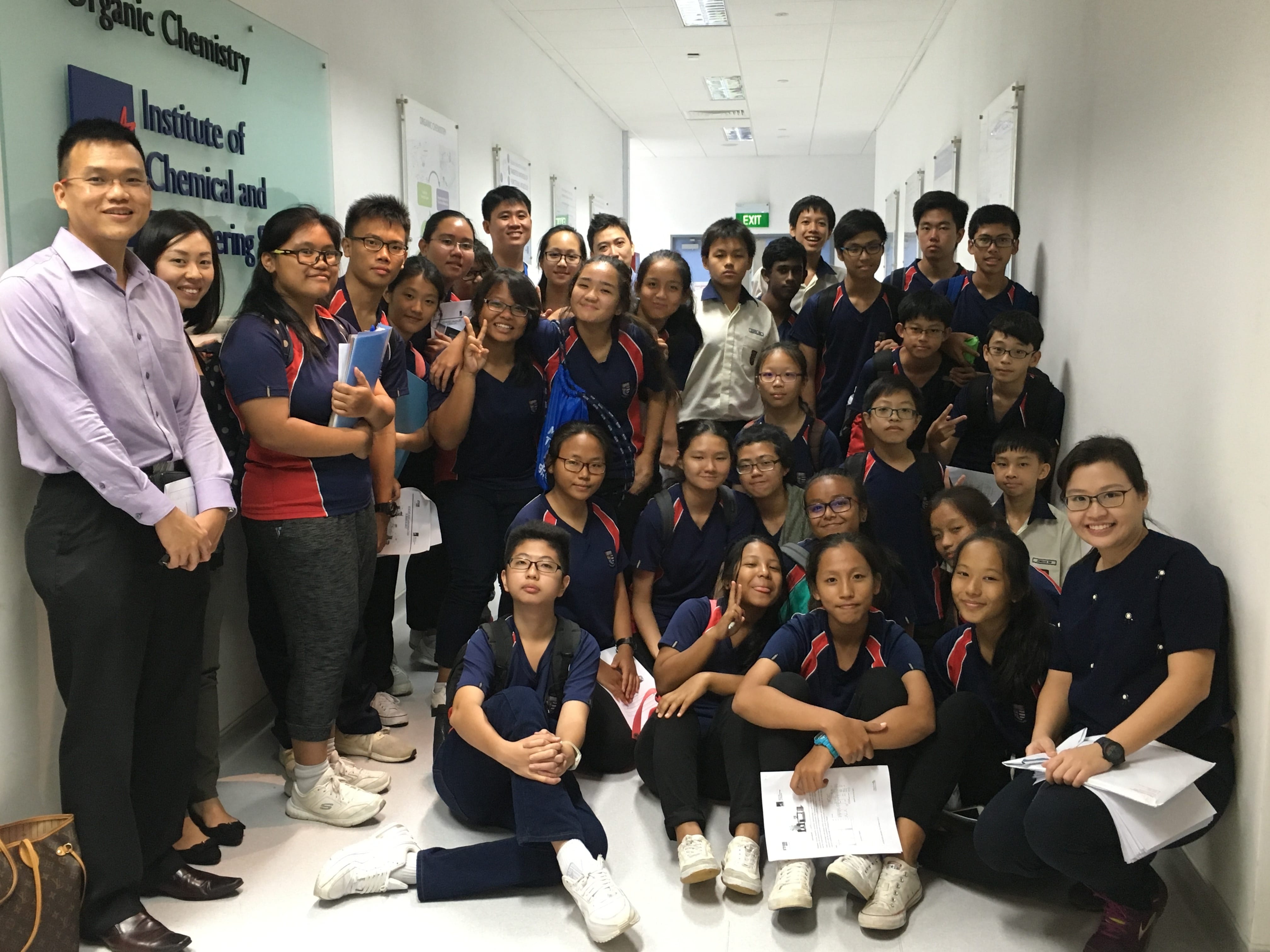A large group of students in navy uniforms pose in a hallway at the Institute of Chemical and Engineering Sciences.